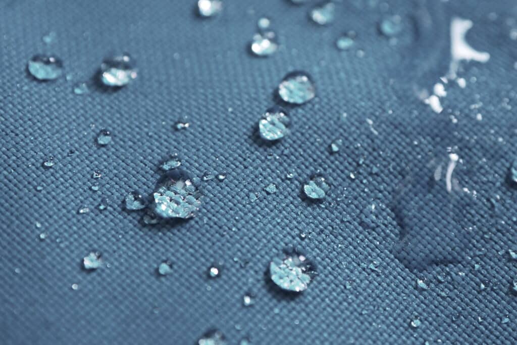 Closeup of water drops on dark blue and grey fabric with waterpr