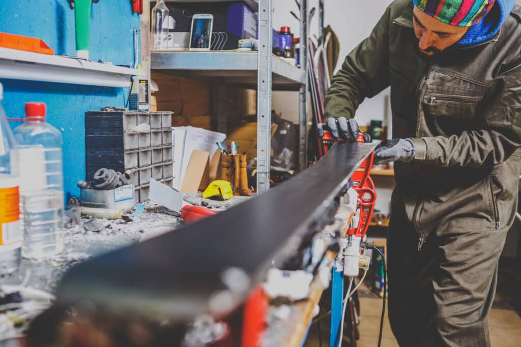 A male worker in a ski service workshop repairs the sliding surface of the skis. Close up of a hand with a plastic scrapper for removing wax, removing new wax. Theme repair of ski curb