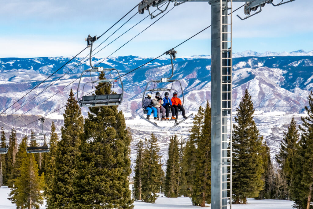 Skiers and snowboarders ascend the Alpine Springs chairlift at the Aspen Snowmass ski resort in the Rocky Mountains of Colorado on a partly cloudy winter day